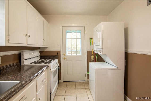 kitchen featuring light tile patterned floors, white range with gas cooktop, stacked washer and clothes dryer, white cabinetry, and a sink