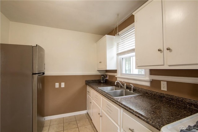 kitchen with a sink, dark countertops, freestanding refrigerator, white cabinets, and light tile patterned floors