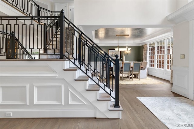 stairway with a decorative wall, a wainscoted wall, wood finished floors, a tray ceiling, and crown molding