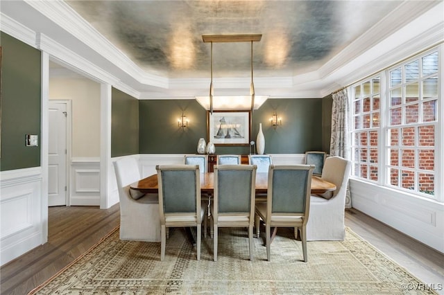 dining room with a wainscoted wall, a raised ceiling, ornamental molding, and wood finished floors