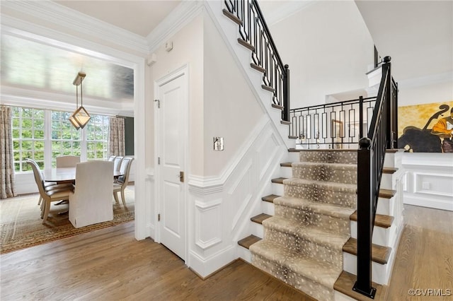 stairs with ornamental molding, a decorative wall, and wood finished floors