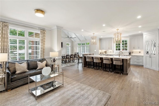 living room featuring crown molding, light wood finished floors, recessed lighting, lofted ceiling, and ceiling fan with notable chandelier