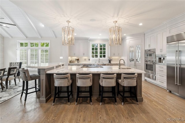 kitchen with a notable chandelier, appliances with stainless steel finishes, white cabinets, and a sink