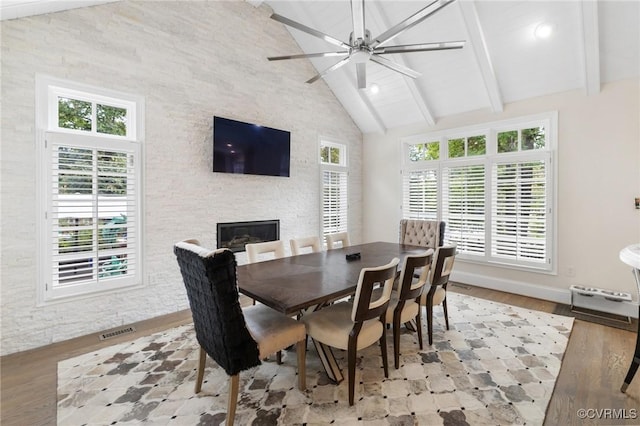 dining room featuring high vaulted ceiling, a ceiling fan, a fireplace, and wood finished floors