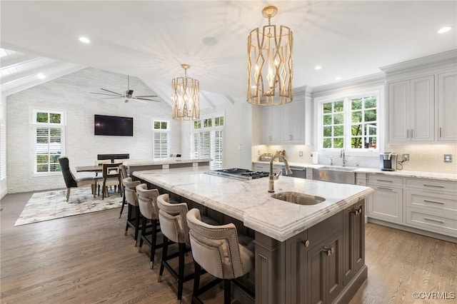 kitchen featuring vaulted ceiling, light stone counters, wood finished floors, and stainless steel gas stovetop