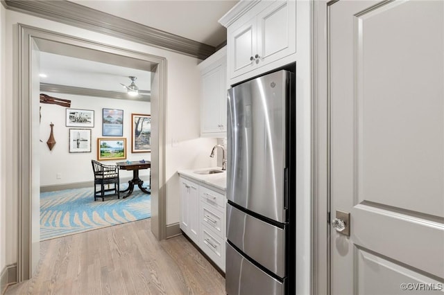 kitchen with freestanding refrigerator, white cabinetry, crown molding, and a sink