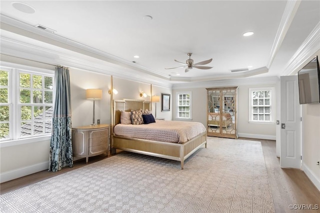 bedroom featuring a tray ceiling, multiple windows, and crown molding