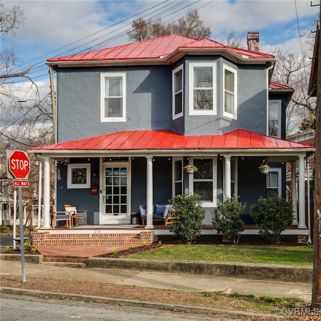 view of front of home with a standing seam roof, a porch, stucco siding, a chimney, and metal roof