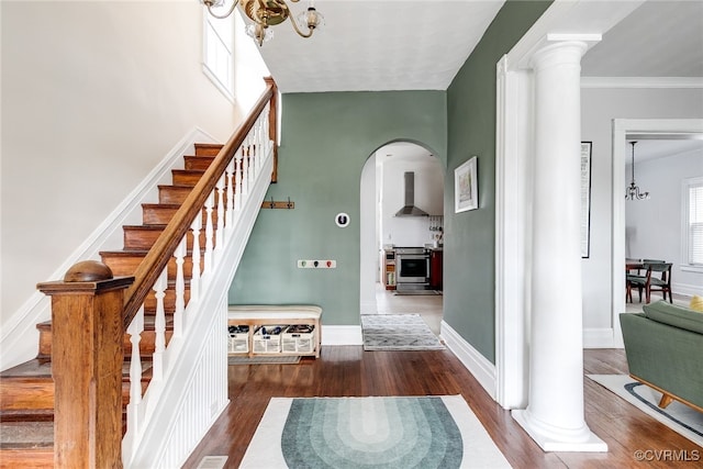 staircase featuring arched walkways, a notable chandelier, wood finished floors, and decorative columns