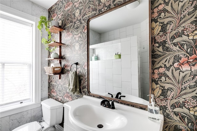 bathroom featuring a sink, toilet, and wallpapered walls