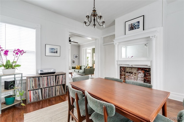 dining space featuring a chandelier, wood finished floors, a fireplace, and crown molding