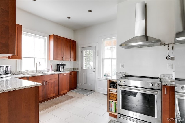 kitchen with wall chimney range hood, brown cabinets, appliances with stainless steel finishes, and a sink