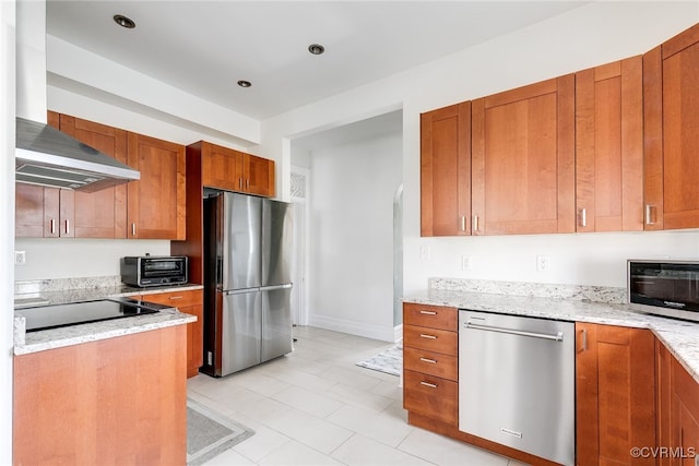 kitchen with light stone counters, brown cabinets, stainless steel appliances, and wall chimney range hood