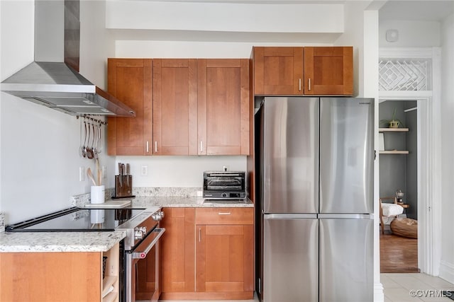 kitchen with light stone counters, appliances with stainless steel finishes, wall chimney exhaust hood, brown cabinetry, and a toaster