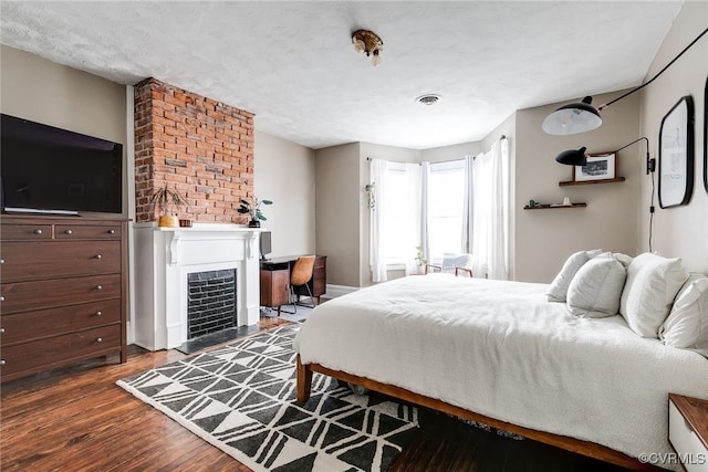 bedroom with a fireplace with flush hearth, wood finished floors, and a textured ceiling