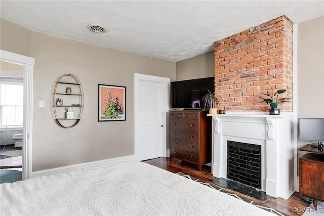 bedroom featuring visible vents, baseboards, dark wood-style floors, and a fireplace