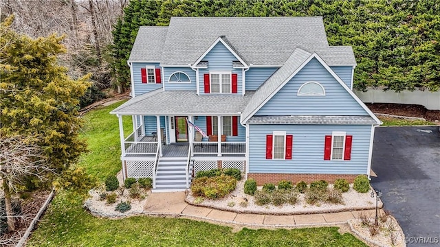 traditional-style home featuring driveway, covered porch, a shingled roof, stairs, and a front lawn