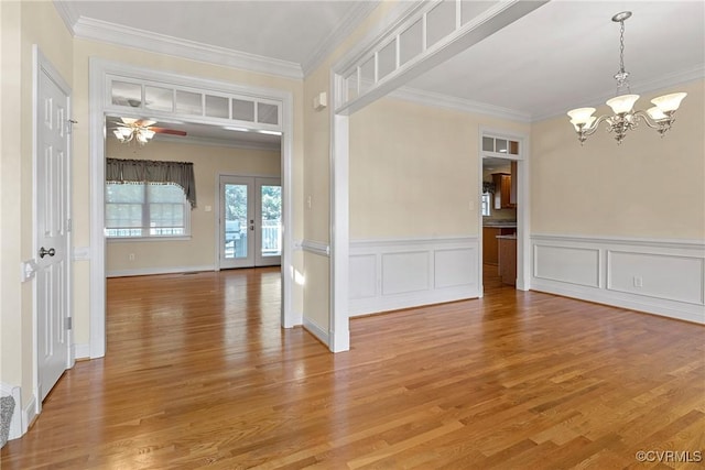 empty room featuring light wood-style flooring, french doors, ceiling fan with notable chandelier, and crown molding