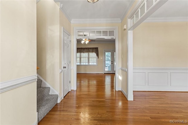 corridor featuring crown molding, stairway, wainscoting, wood finished floors, and a decorative wall