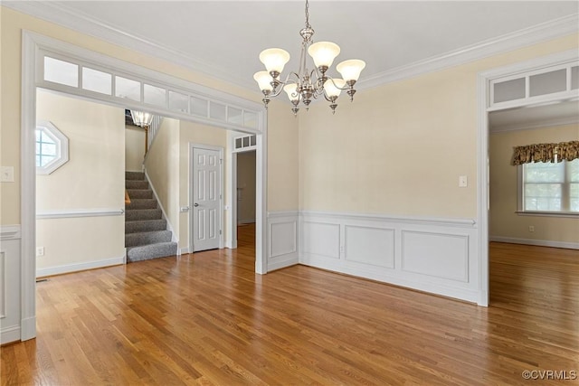 empty room featuring a chandelier, light wood-style flooring, crown molding, and stairs