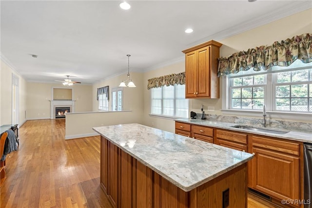 kitchen featuring a warm lit fireplace, a sink, dishwasher, crown molding, and a center island