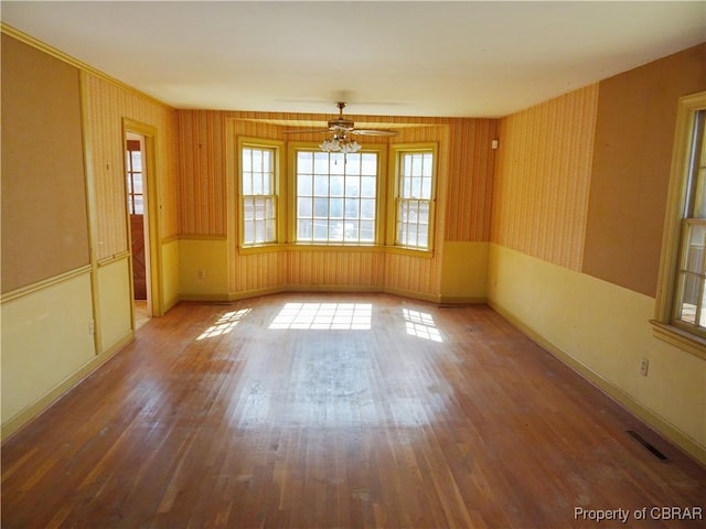 spare room featuring wood finished floors, visible vents, baseboards, and wallpapered walls