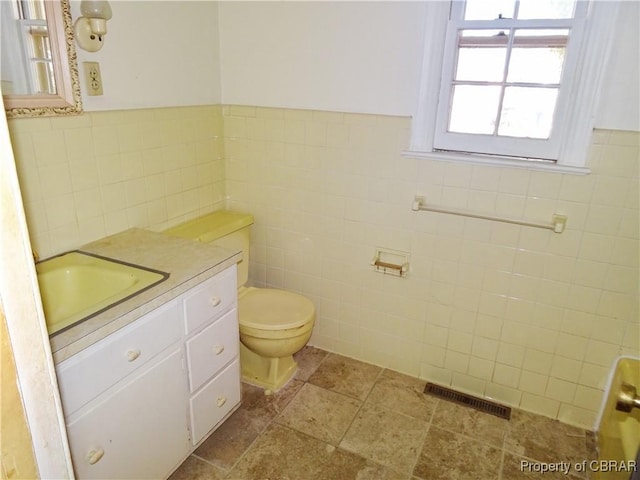 bathroom featuring a wainscoted wall, tile walls, visible vents, toilet, and vanity