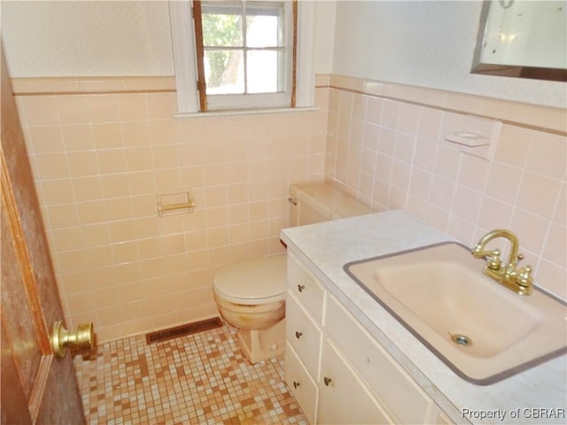 bathroom featuring a wainscoted wall, tile walls, toilet, vanity, and tile patterned flooring