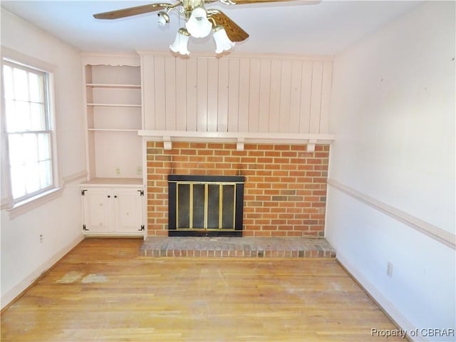 unfurnished living room with a ceiling fan, baseboards, built in features, light wood-type flooring, and a brick fireplace