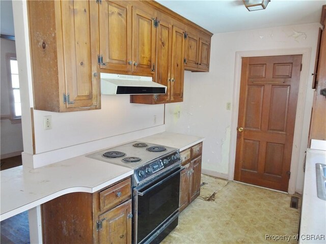 kitchen with electric range, brown cabinets, light floors, light countertops, and under cabinet range hood