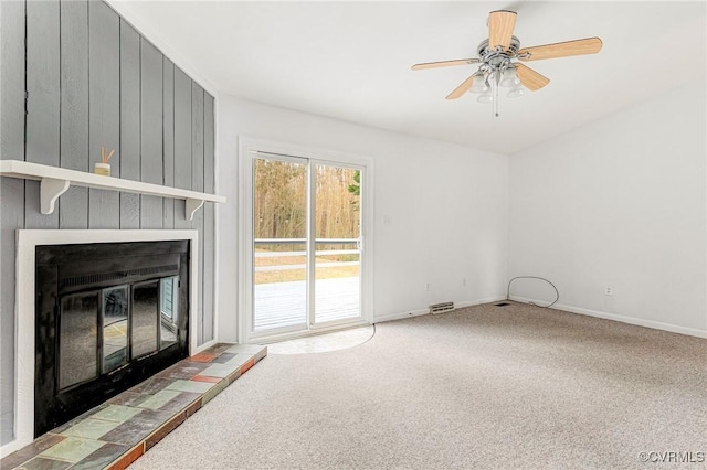 unfurnished living room featuring a tile fireplace, baseboards, ceiling fan, and carpet floors