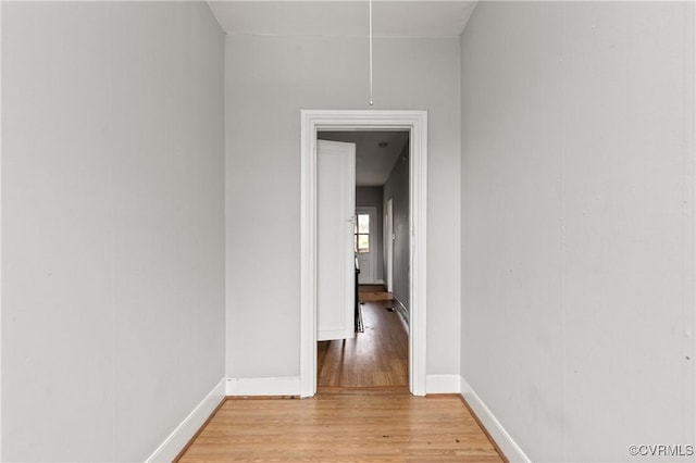 hallway with light wood finished floors, attic access, and baseboards