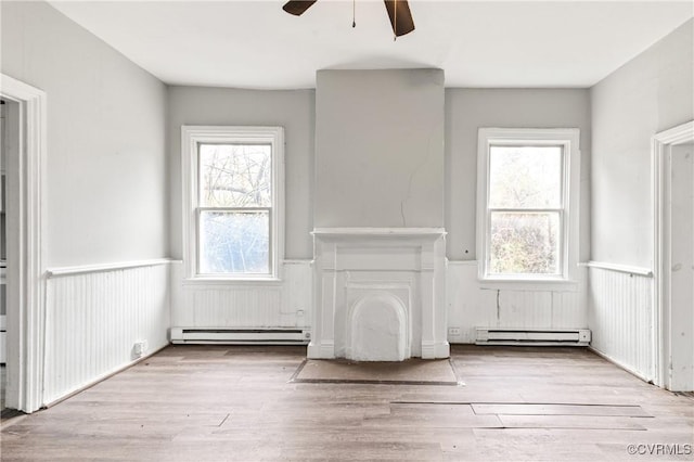 unfurnished living room with baseboard heating, wainscoting, and wood finished floors