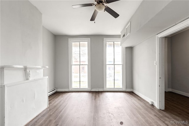 empty room featuring a baseboard heating unit, wood finished floors, a ceiling fan, and baseboards