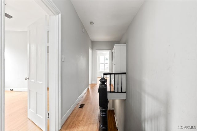 hallway with light wood-style flooring, visible vents, baseboards, and an upstairs landing