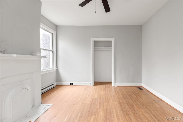 unfurnished bedroom with light wood finished floors, a closet, baseboard heating, a ceiling fan, and baseboards