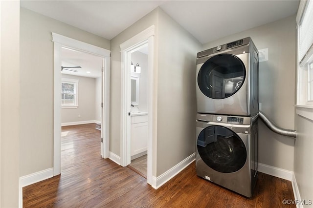 washroom featuring stacked washing maching and dryer, baseboards, and wood finished floors