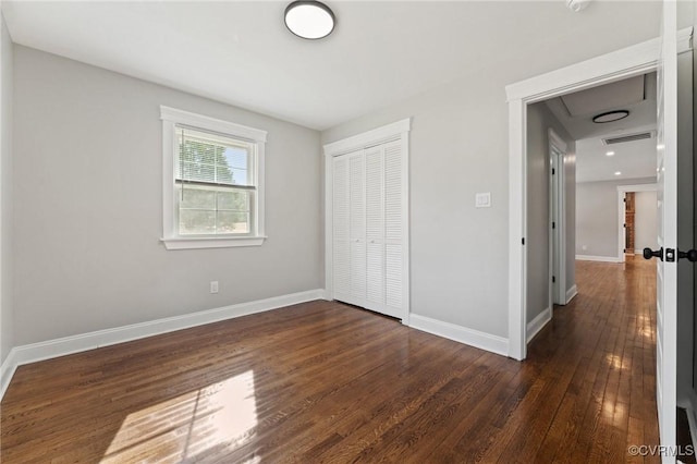 unfurnished bedroom featuring dark wood-style flooring, a closet, visible vents, and baseboards