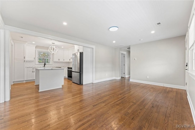 unfurnished living room featuring light wood-style floors, recessed lighting, a sink, and baseboards