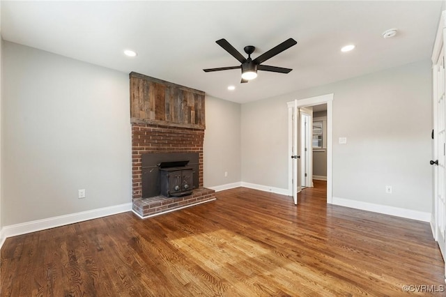 unfurnished living room featuring recessed lighting, wood finished floors, a wood stove, and baseboards