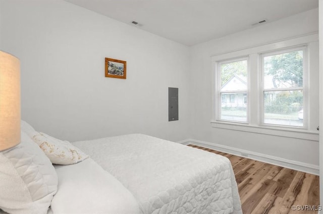 bedroom featuring wood finished floors, electric panel, and baseboards