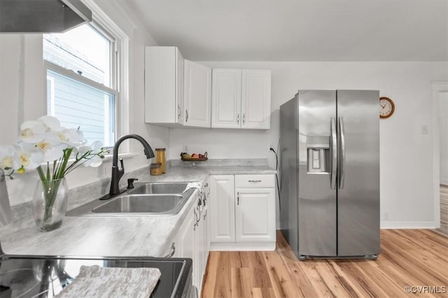 kitchen with light wood-style flooring, stainless steel refrigerator with ice dispenser, a sink, and white cabinetry