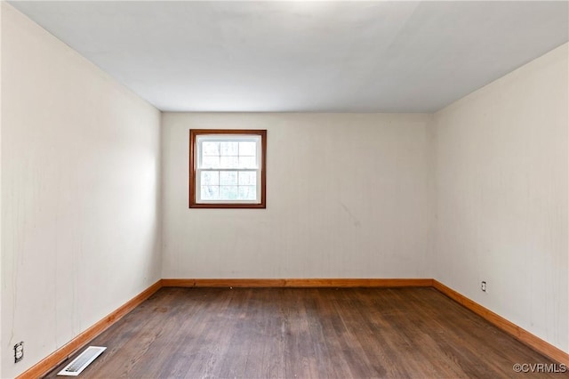 spare room with wood finished floors, visible vents, and baseboards