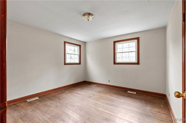 spare room featuring wood finished floors, visible vents, and baseboards