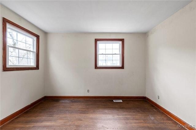 spare room with a wealth of natural light, visible vents, and wood finished floors