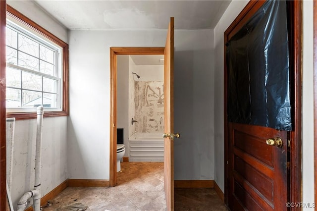 bathroom with toilet, shower / tub combination, and baseboards