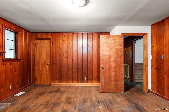 spare room with baseboards, wood-type flooring, visible vents, and wooden walls