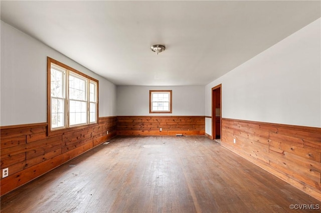 unfurnished room with hardwood / wood-style flooring, wooden walls, and wainscoting