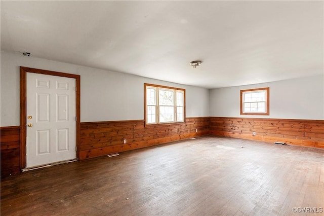 unfurnished room featuring a wealth of natural light, wainscoting, wooden walls, and wood finished floors