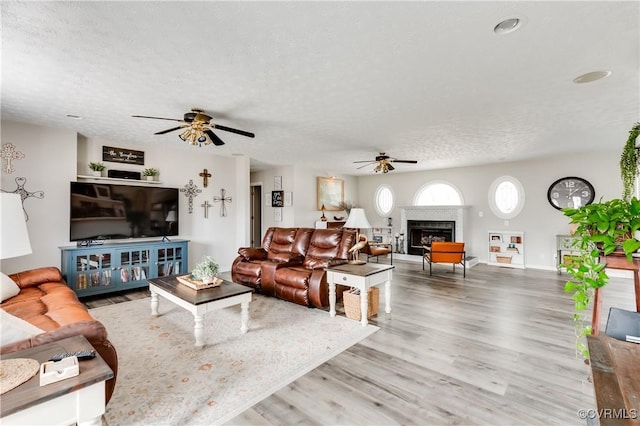 living room with a ceiling fan, a textured ceiling, wood finished floors, and a fireplace